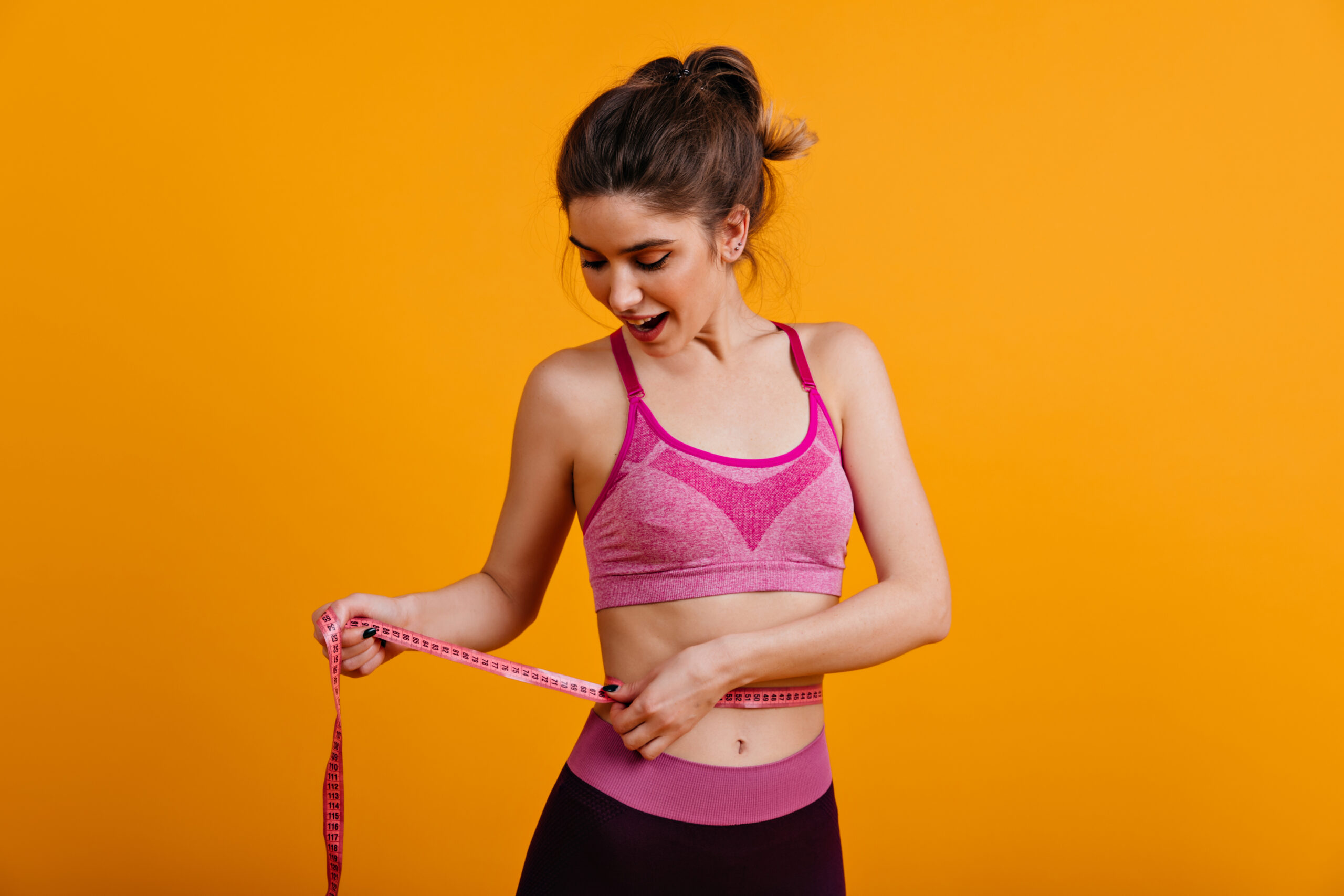 Charming Young Woman Taking Measurements Of Her Body. Sporty Girl Posing In Pink Clothes