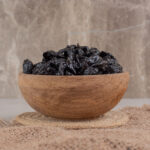 Dry Black Plums In A Wooden Cup On A Piece Of Burlap