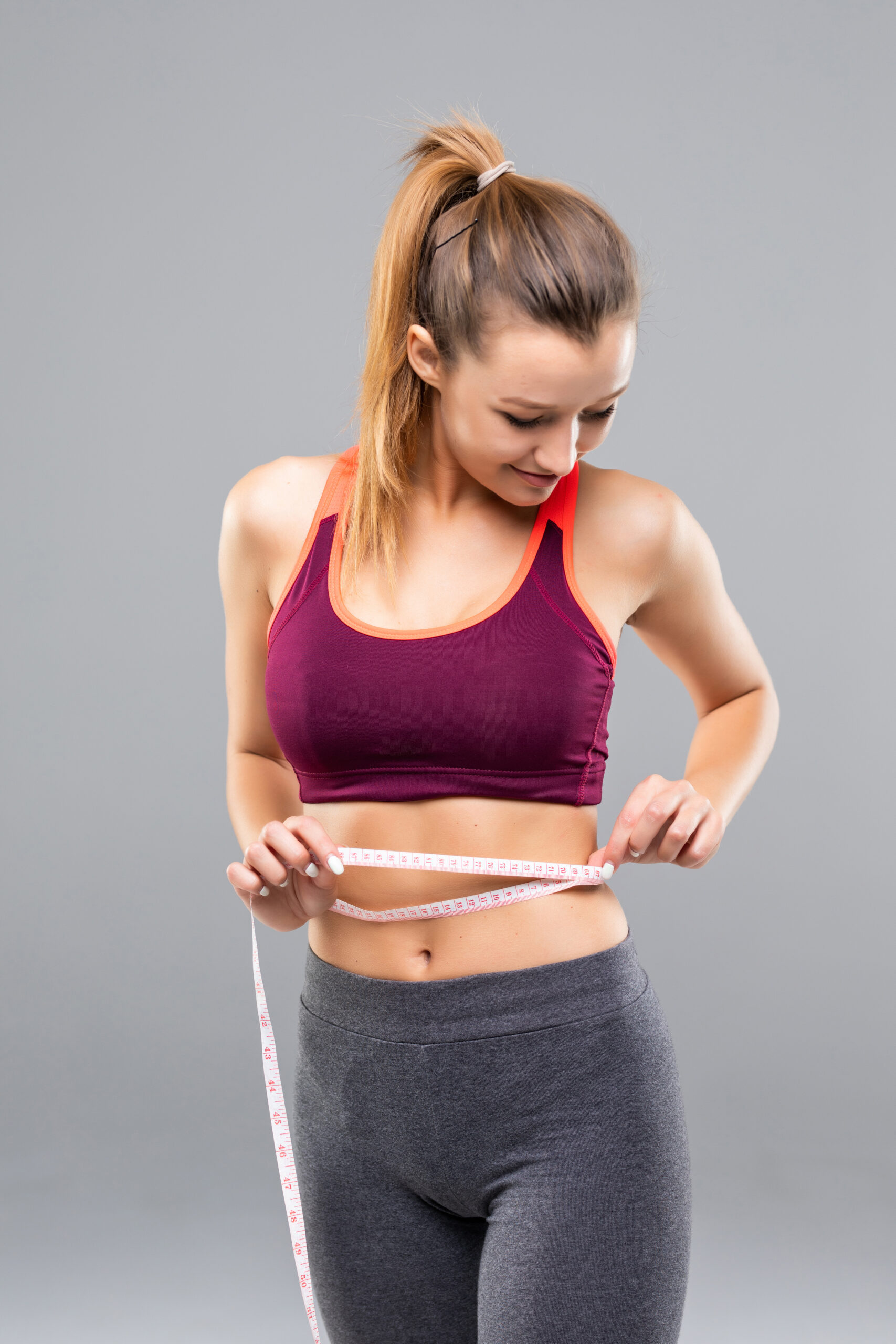 Fitness Woman Measuring Her Body Isolated On Gray Background. Weight Loss Concepts