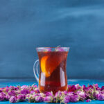 Glass Of Tea With Budding Roses Placed On Blue Background