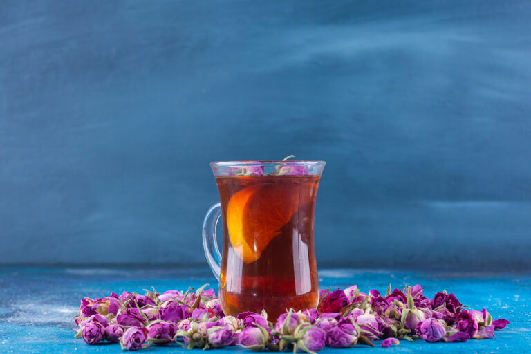 Glass Of Tea With Budding Roses Placed On Blue Background