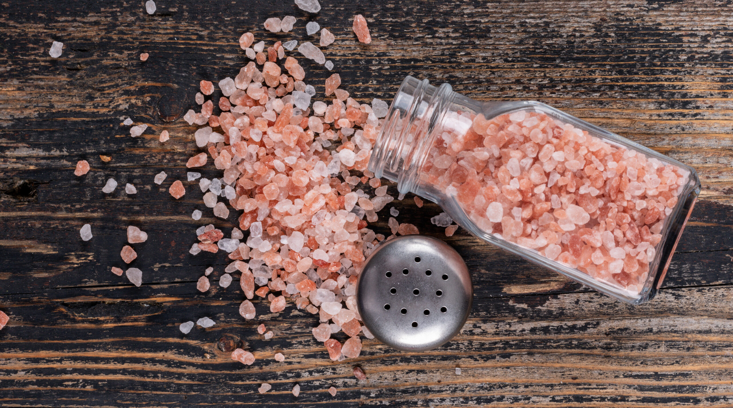 Himalayan Salt Coming Out Of Open Salt Shaker On A Dark Wooden Background. Top View.